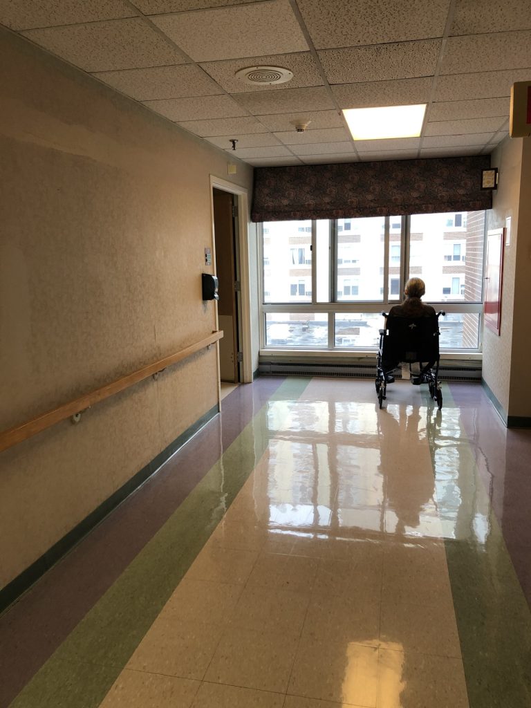 elderly man in wheel chair at the end of a long lonely hallway. 